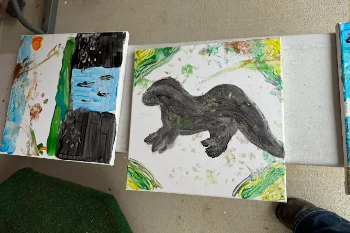 Two abstract paintings; left shows colorful shapes, right features a dark creature silhouette with green accents.