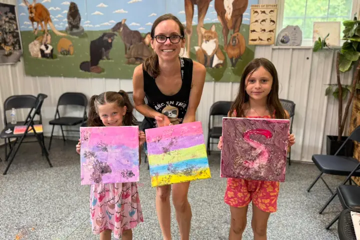 Woman with two girls showing colorful paintings in art studio.